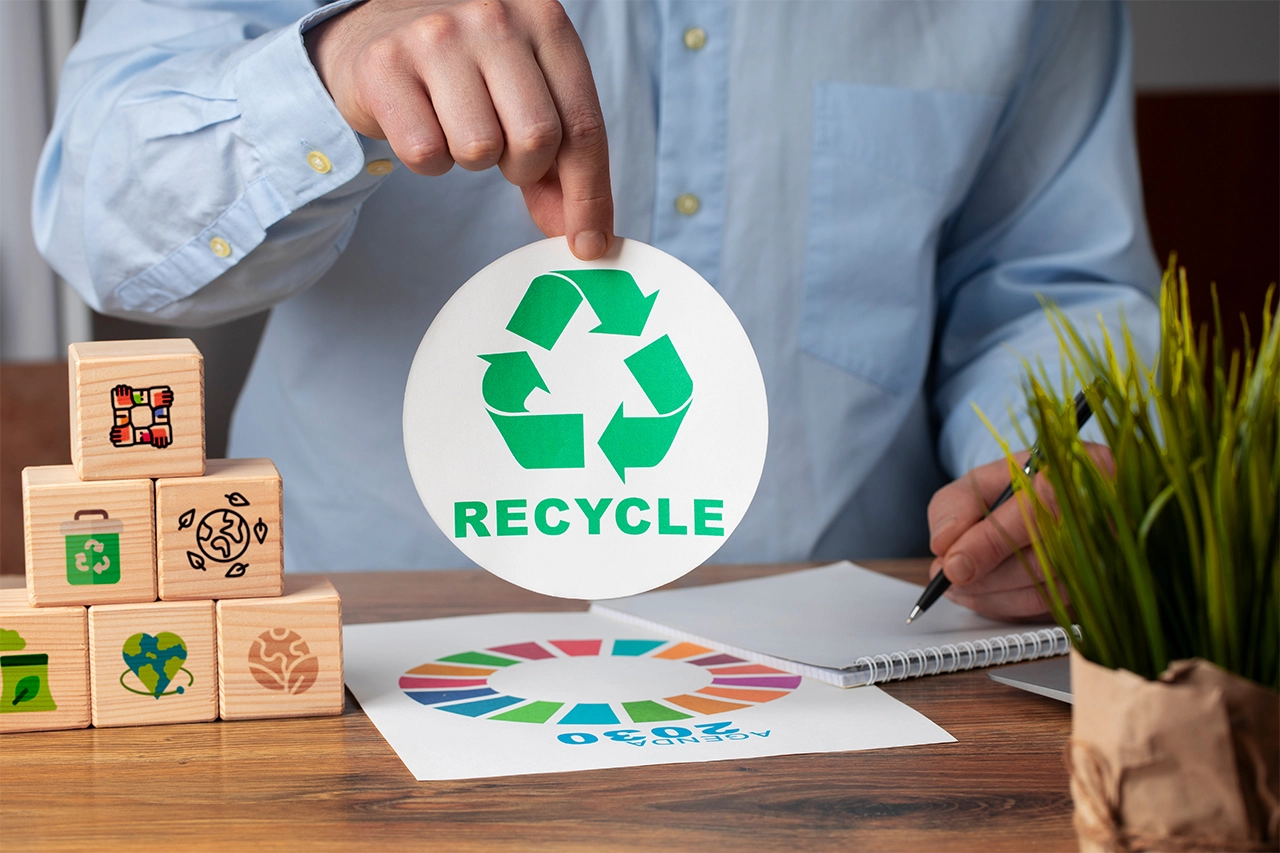 Person holding recycle symbol while planning sustainable packaging strategy with eco-friendly icons and circular economy concept on desk