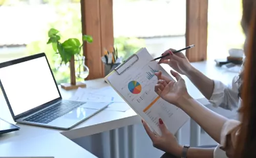 Two people discussing assessment report with charts beside a laptop at desk