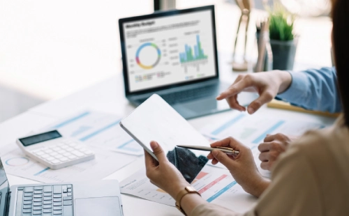 People collaborating with reports, tablet and laptop showing business capability graphs