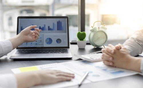 Two people discussing market data with graphs and reports at modern office desk