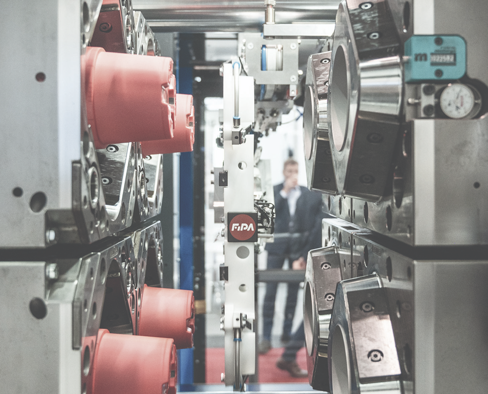 Robotic arm operating between open metal molds, transferring red plastic products in a high-tech automated manufacturing process.