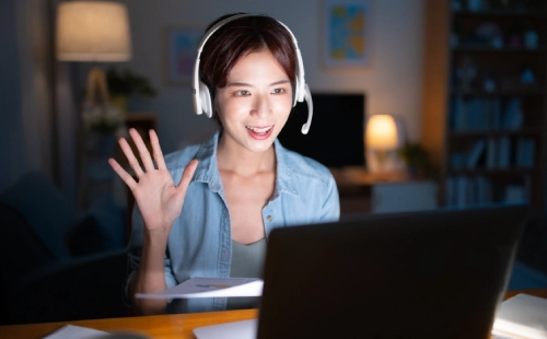 Woman wearing headset participating in virtual video call at night with laptop