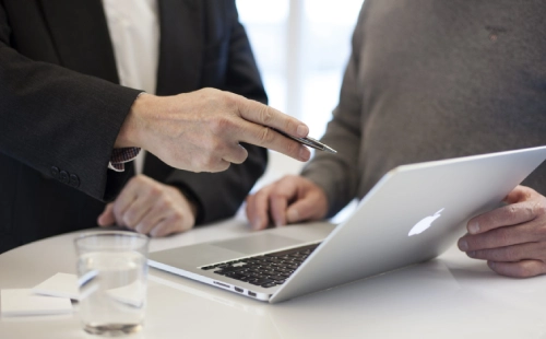 Close-up of two people sharing ideas and pointing at MacBook screen in meeting