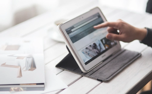 Hand operating procurement portal on tablet with digital documents on table