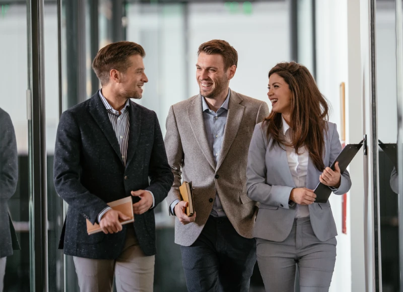 Three business professionals walking and talking in a modern glass office.